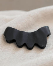 Macro close-up of one black KinetiPath Reflex toe spacer on linen, showing the four rounded toe lobes
