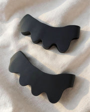 KinetiPath Reflex toe spacers in black, a mirrored pair lying on warm linen in soft morning light