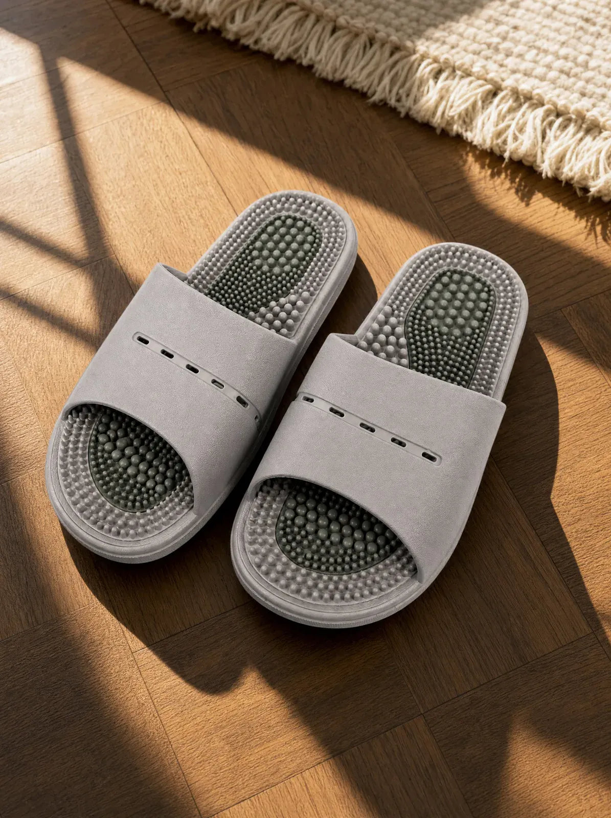 Meridian men's reflexology slides in light grey with a green footbed, on a warm oak floor beside a linen rug