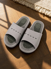 Meridian men's reflexology slides in light grey with a green footbed, on a warm oak floor beside a linen rug
