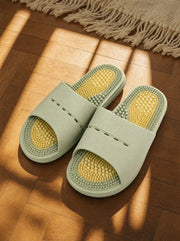 Meridian women's reflexology slides in sage green, resting on a warm oak floor beside a linen rug in morning light