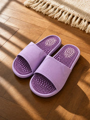 Zenith women's reflexology slides in lilac with a purple footbed, on a warm oak floor beside a linen rug